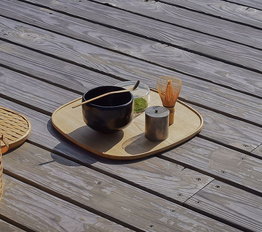 Tray with a black bowl, glass, and candle on a wooden deck