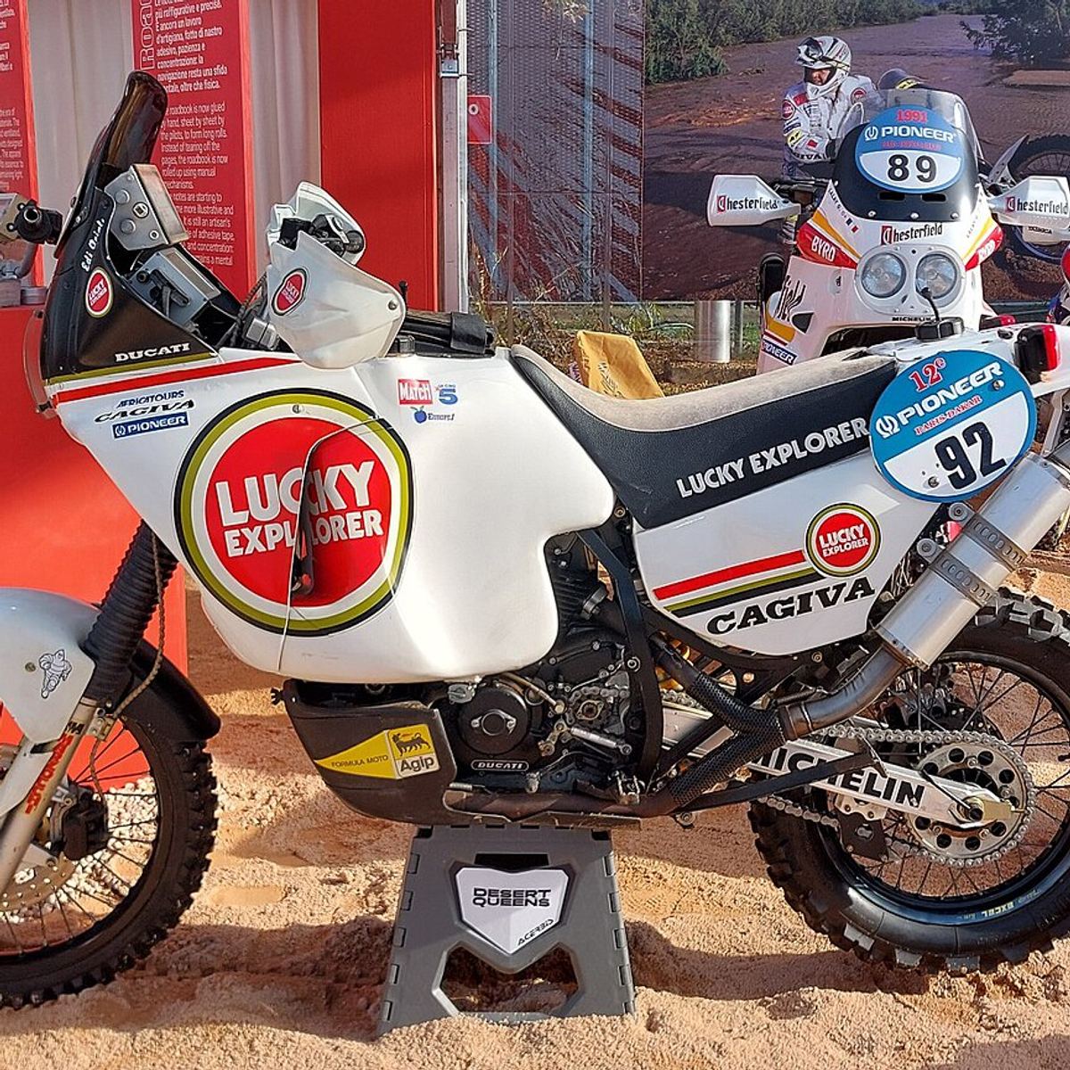 White Cagiva Elefant 900 rally bike in Lucky Explorer livery, displayed on sand as Edi Orioli's 1990 Dakar winner