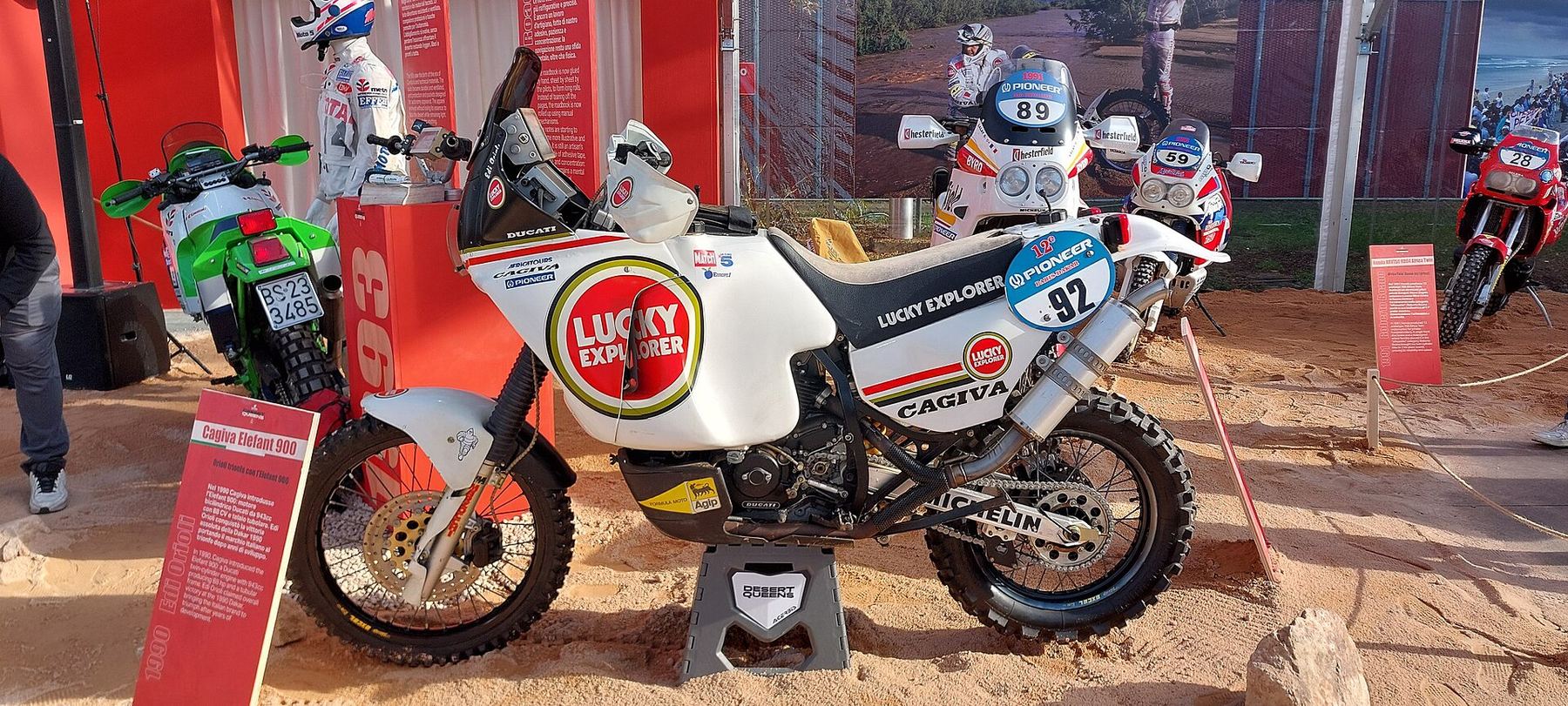 White Cagiva Elefant 900 rally bike in Lucky Explorer livery, displayed on sand as Edi Orioli's 1990 Dakar winner