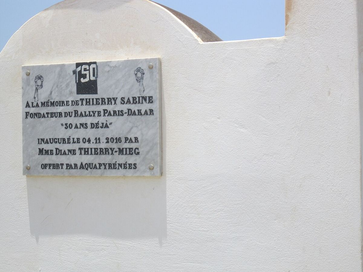 Memorial plaque to Thierry Sabine, founder of the Paris–Dakar Rally, on a white wall at the Lac Rose in Senegal