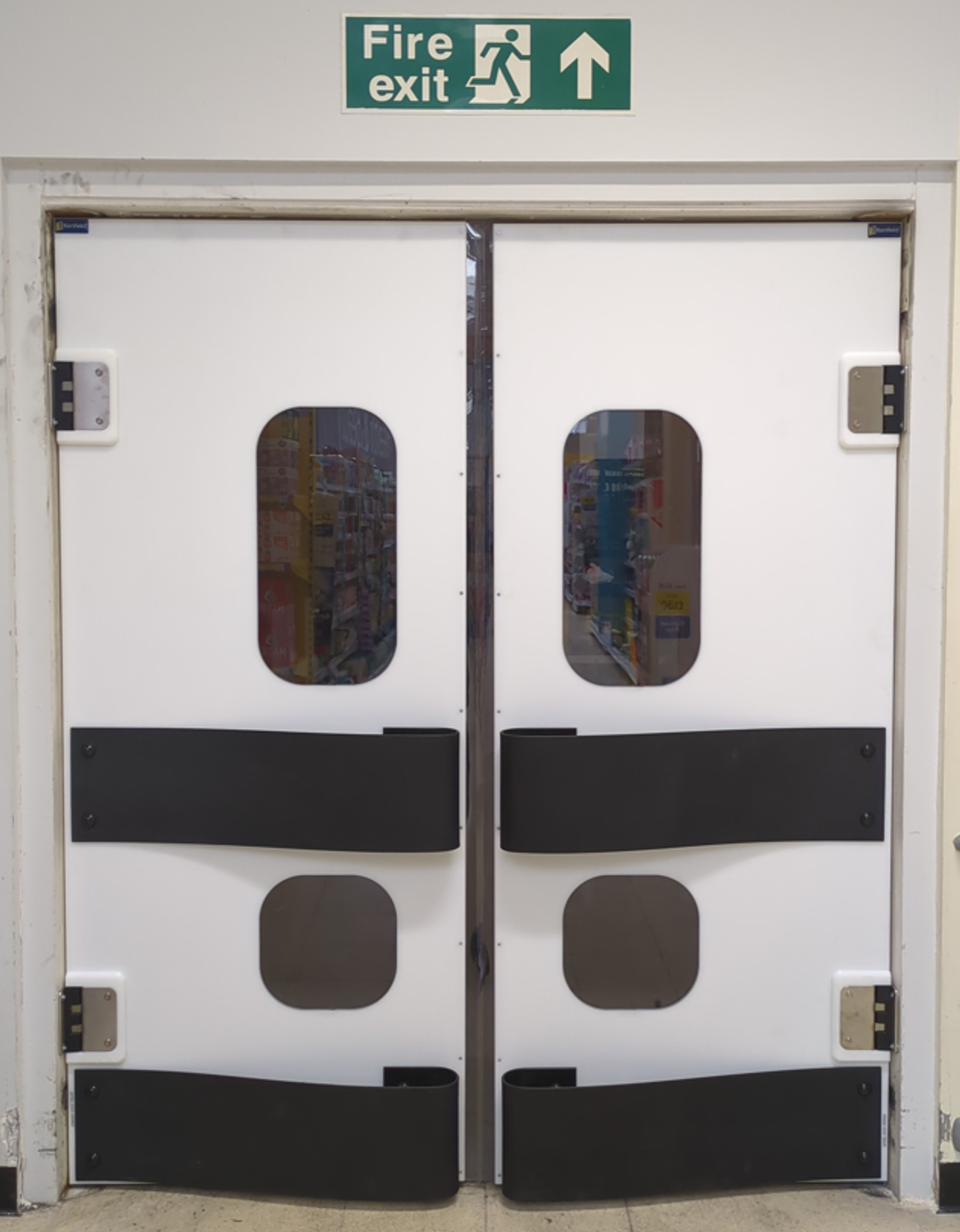 K150 white polyethylene double swing doors under a fire-exit sign in a supermarket back-of-house corridor