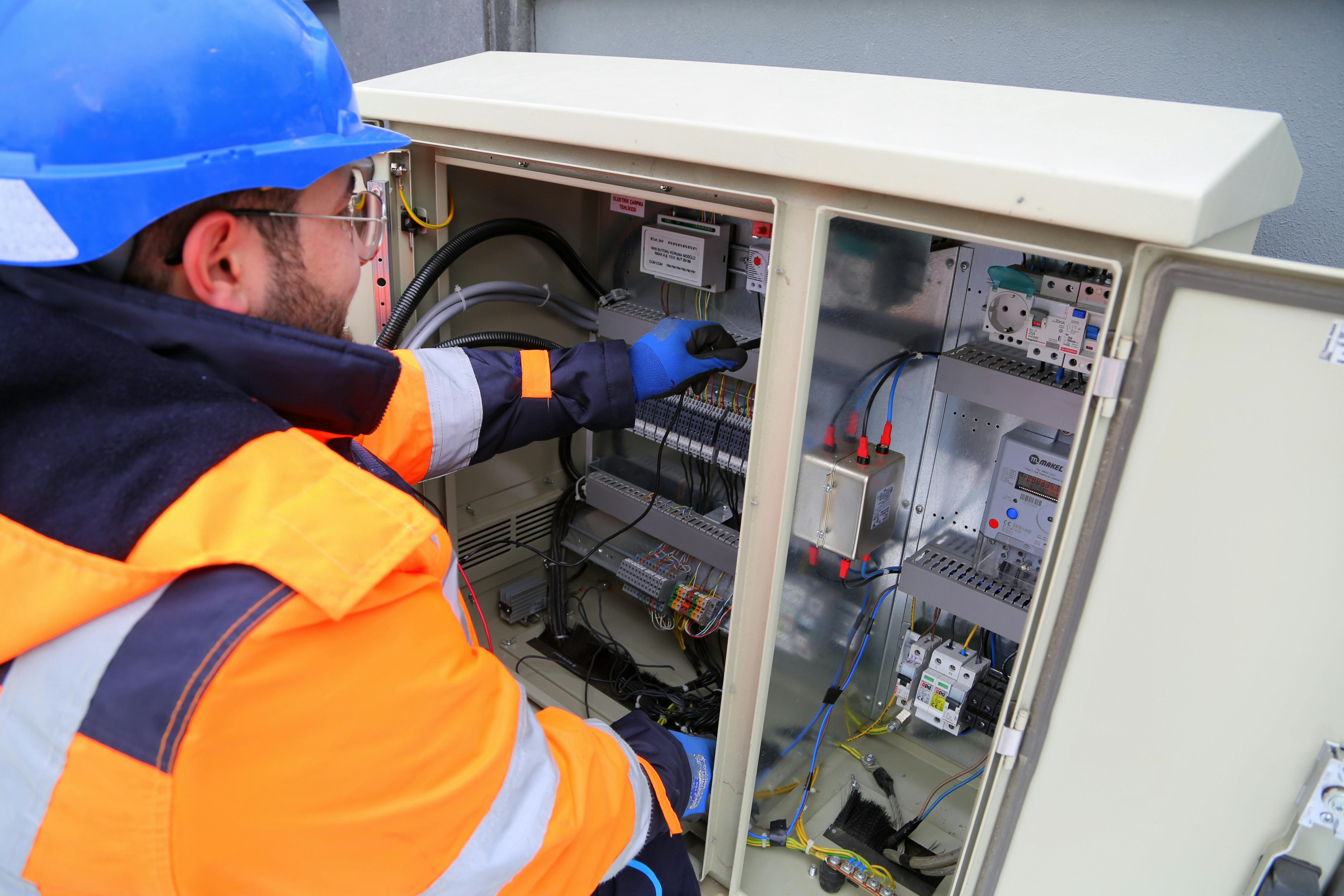 A power load controller closeup image at the construction site and a worker operating it in he orange jacket and a blue helmet