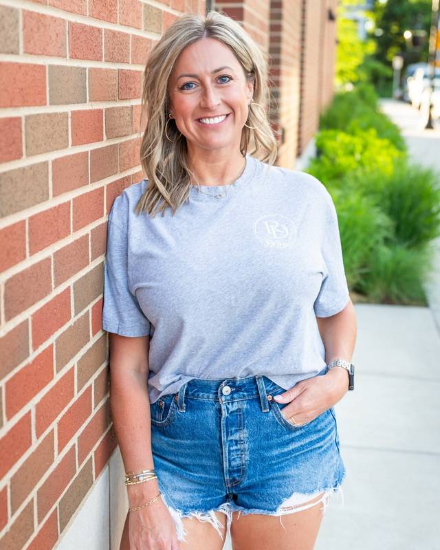 Staci Perkins, founder of Reid Design, smiling outside a brick storefront.