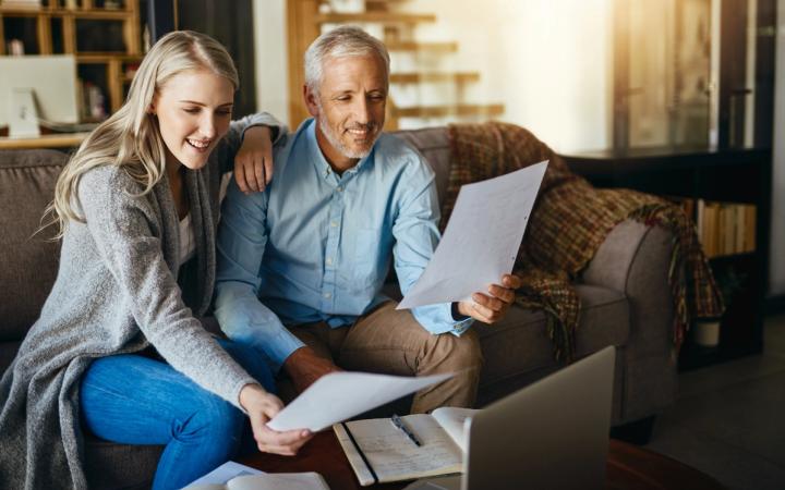 A couple sitting on a sofa reviewing retirement planning documents together with a laptop and notebook on the table.