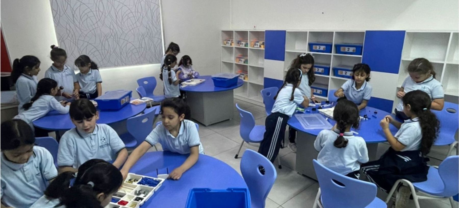 التلاميذ يعملون في مجموعات على الطاولات الزرقاء مع أدواتهم