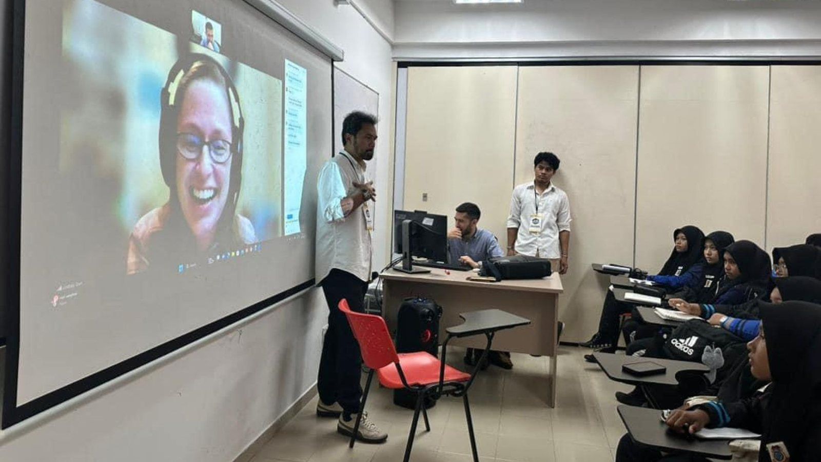مدرسون في قاعة تدريب يشاركون في جلسة مباشرة عبر الإنترنت تُعرض على شاشة كبيرة