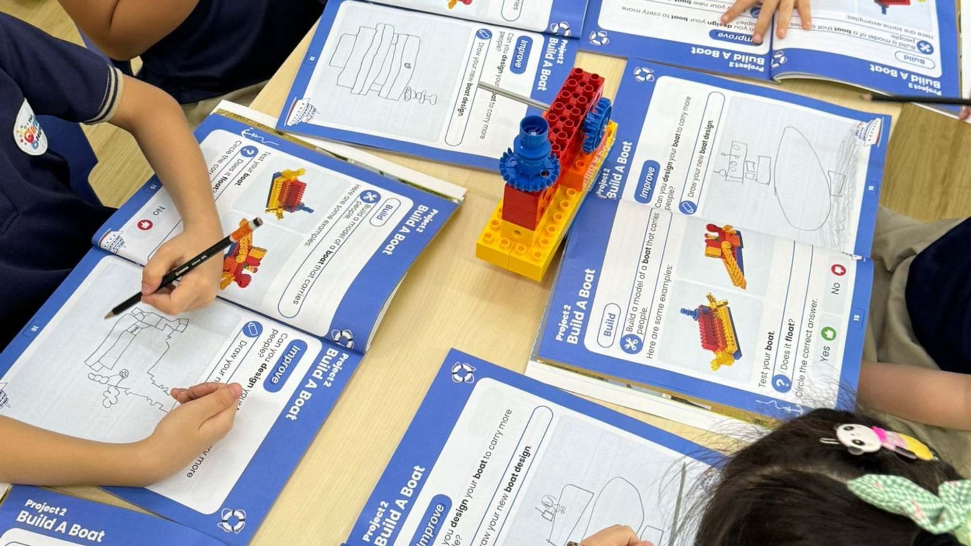 Les élèves de maternelle dessinent leurs projets de bateaux dans leurs cahiers d'exercices, autour d'une maquette qu'ils ont construite, Projet n° 2 : Construire un bateau