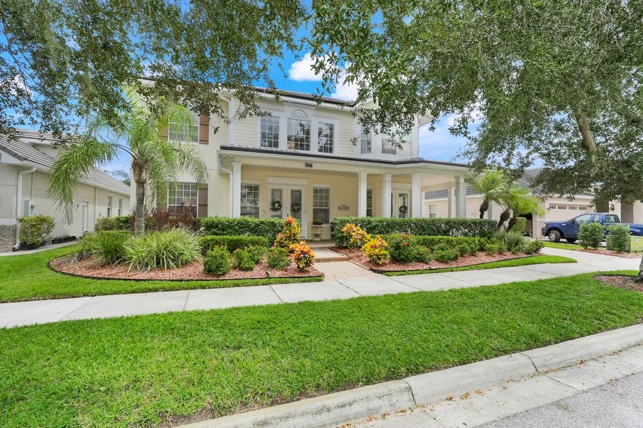 White two-story home with covered front porch, columns, and mature palm trees in an Orlando, Florida neighborhood