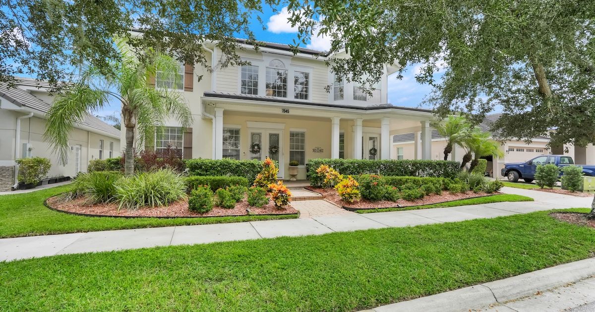 White two-story home with covered front porch, columns, and mature palm trees in an Orlando, Florida neighborhood
