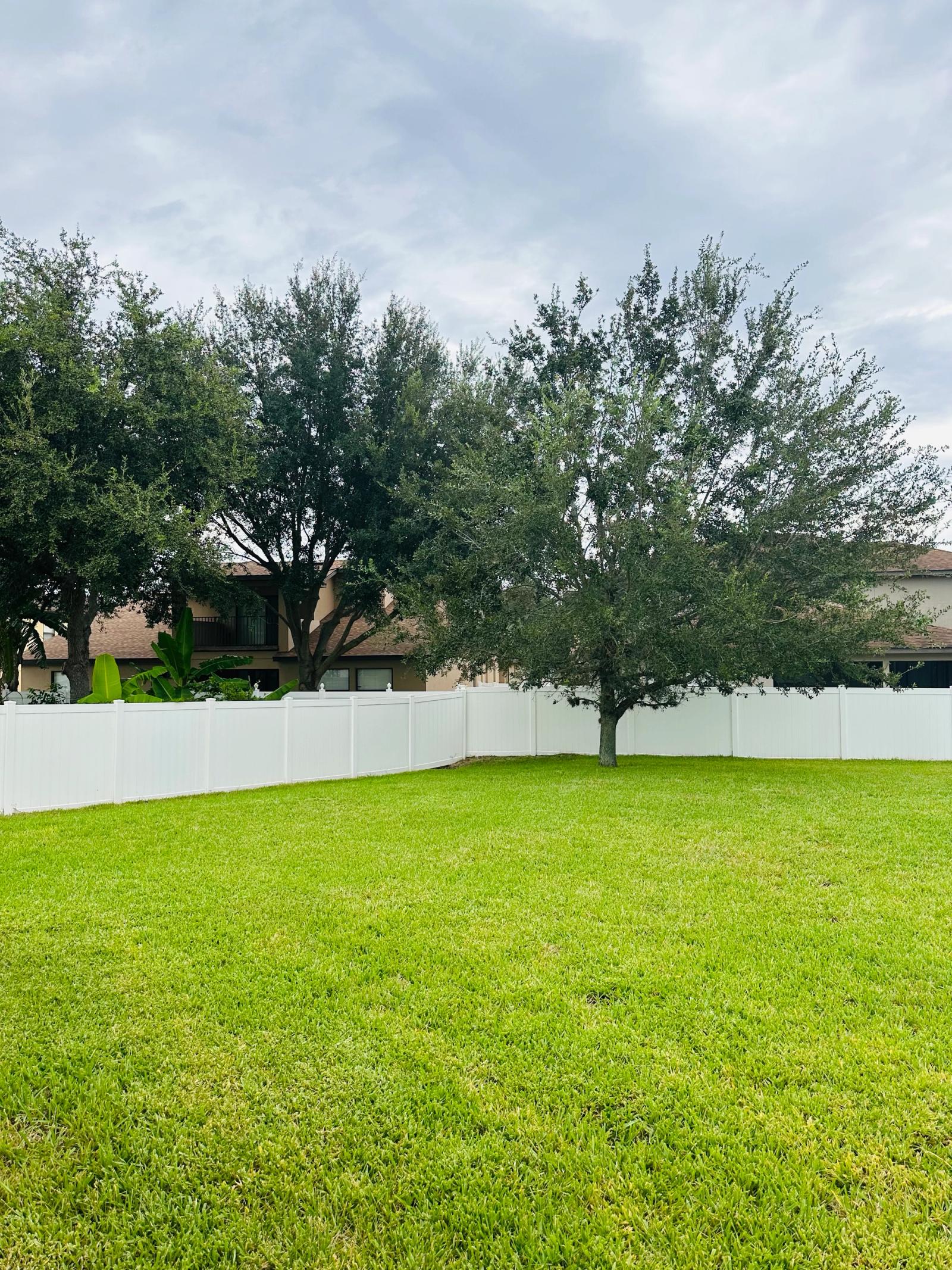 Large fenced-in backyard with mature oak trees and green lawn in a Minneola, Florida new construction community