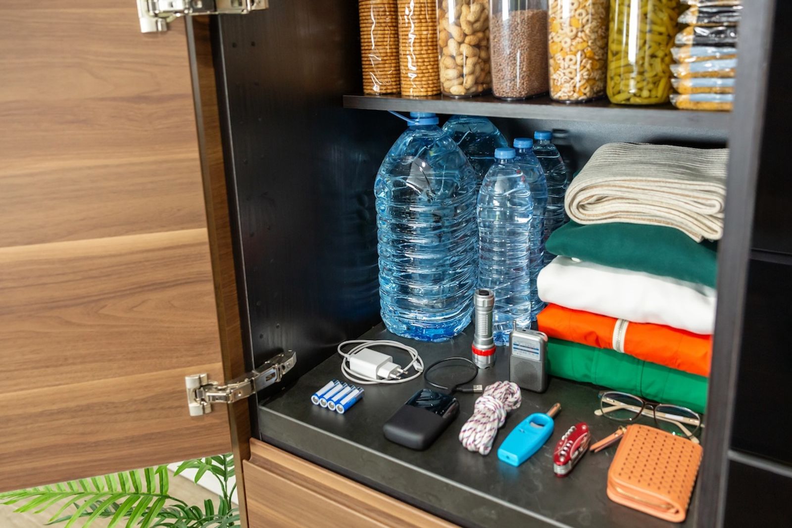 Organized emergency kitchen pantry with water bottles, packaged food, clothes, survival and communications supplies. Stocked cupboard ready as part of alert, foresight and self sufficiency strategy.