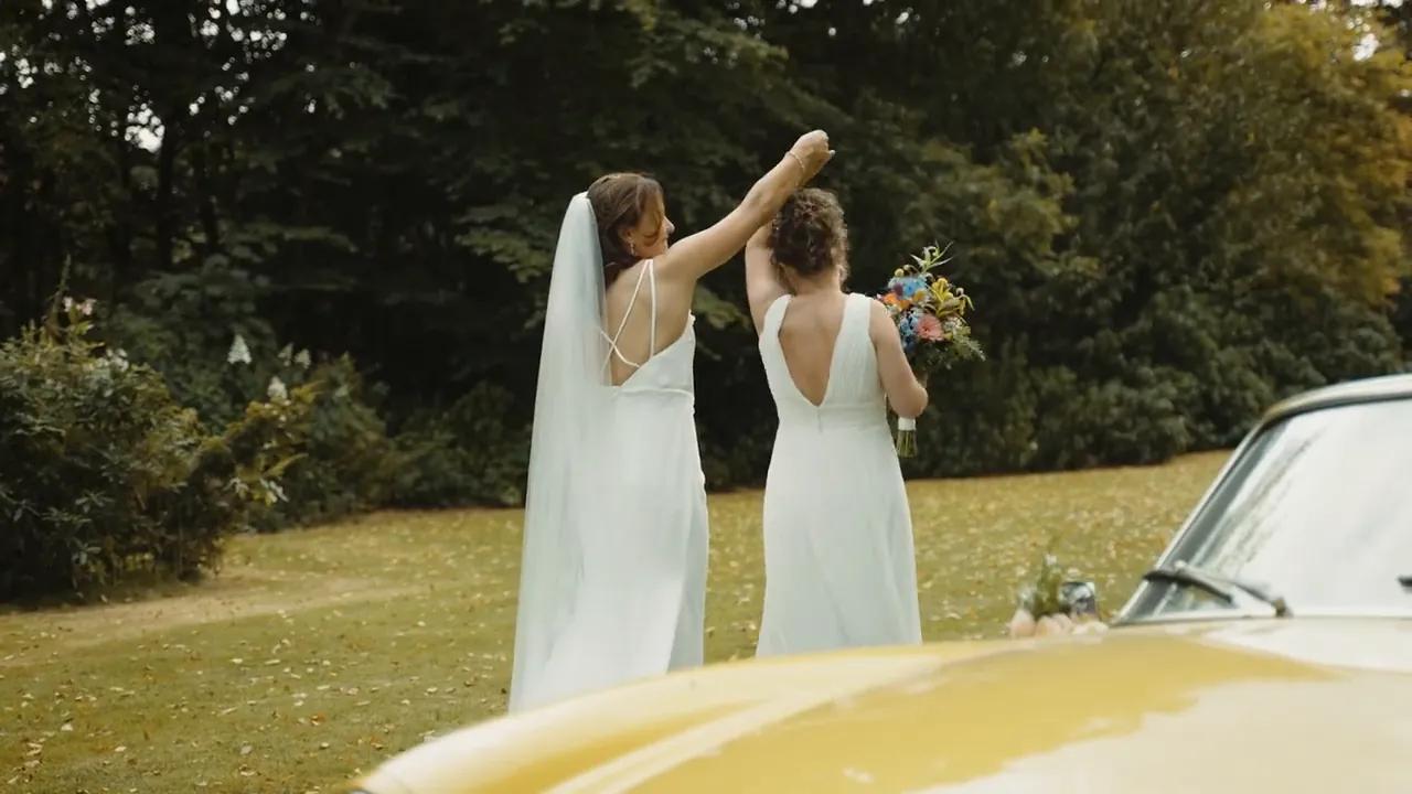 Two brides cheering with their bouquet next to a yellow convertible