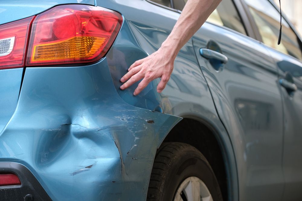 Hand touching dented rear panel of blue car after rideshare accident in New Jersey