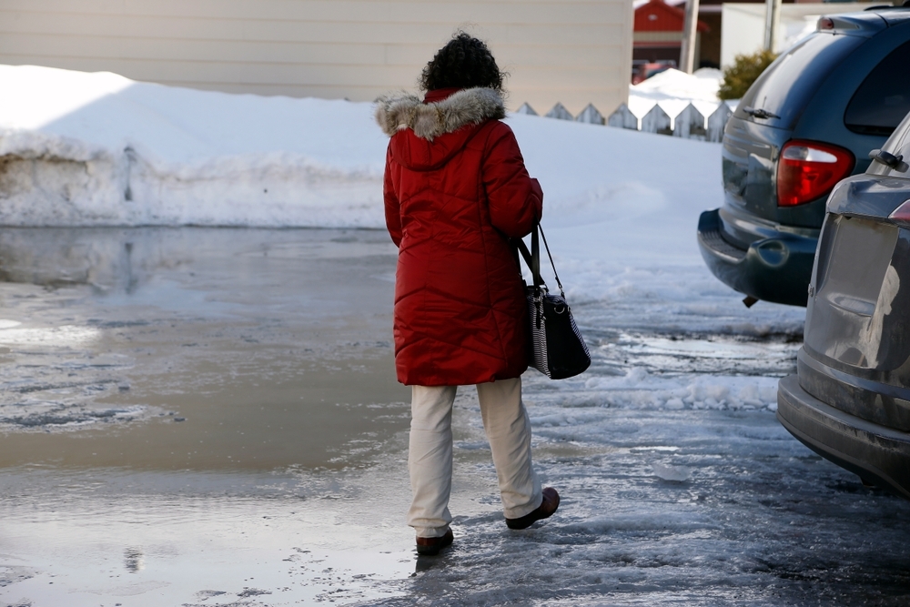 Image A person in a red winter parka walking across a slushy, icy parking lot between parked cars during the winter holiday shopping season.