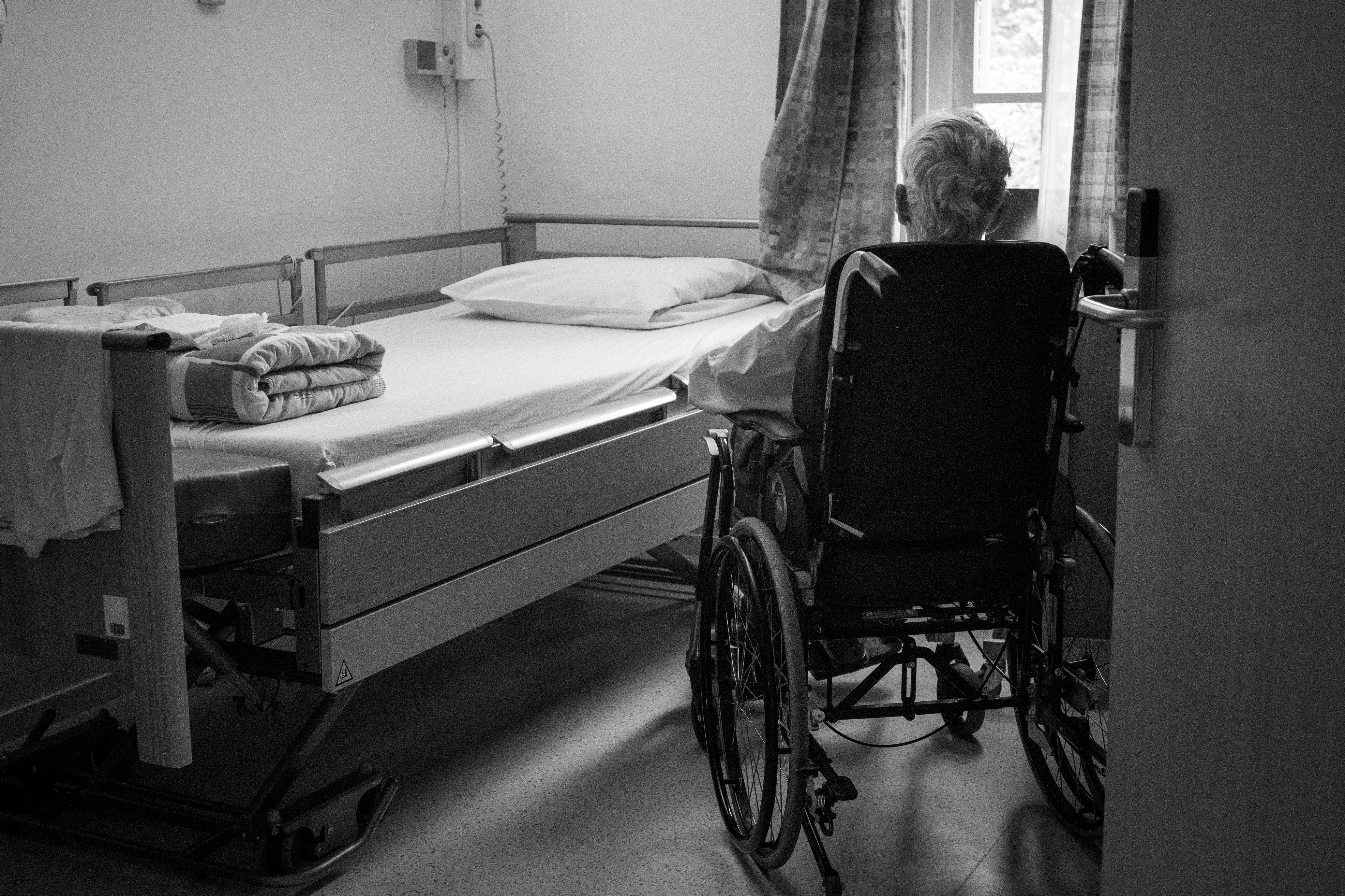 Elderly resident in a wheelchair gazing out the window of a nursing home room, symbolizing red flags of nursing home abuse.
