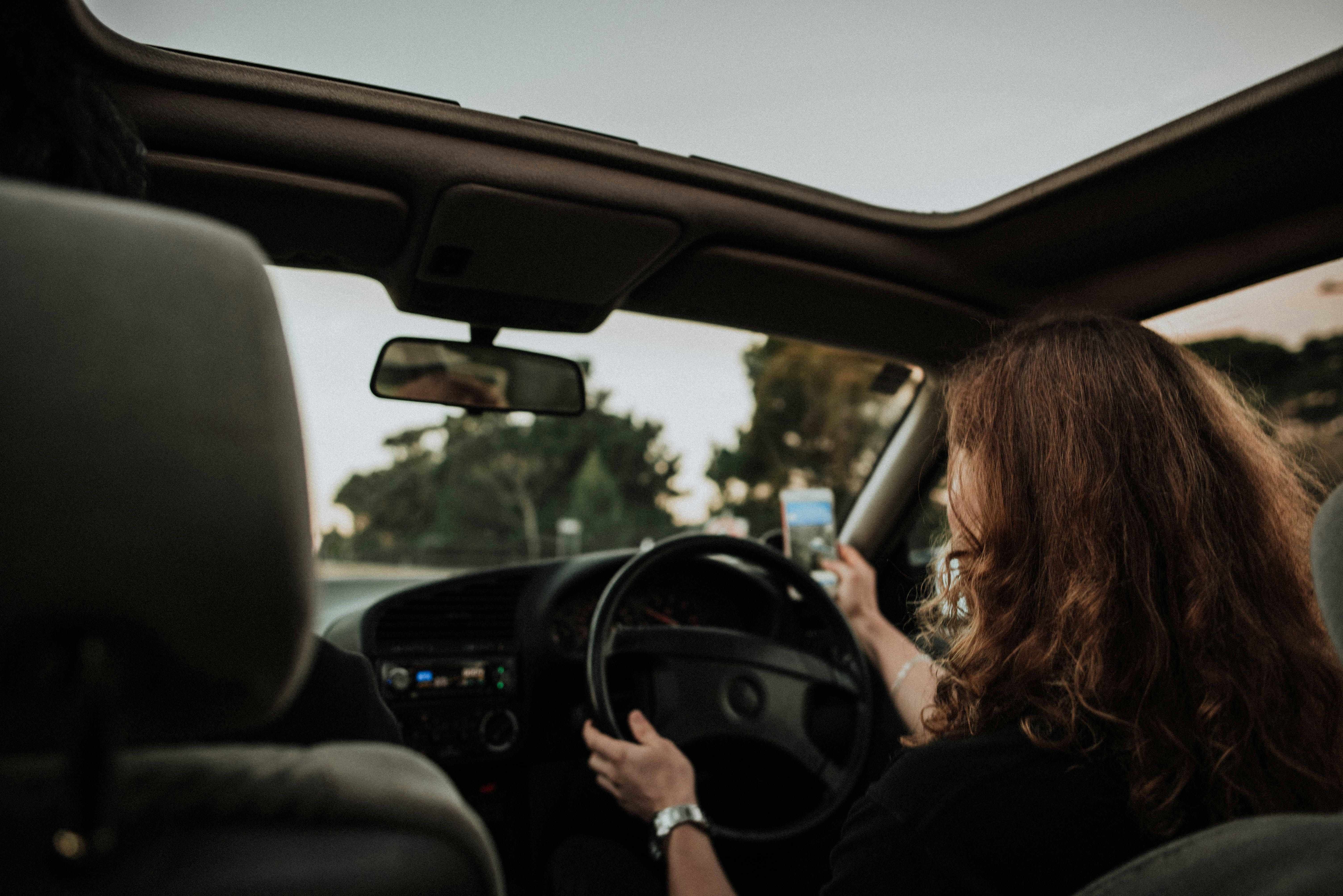 Driver using a phone while driving with one hand on the wheel, showing the dangers of distracted driving accidents