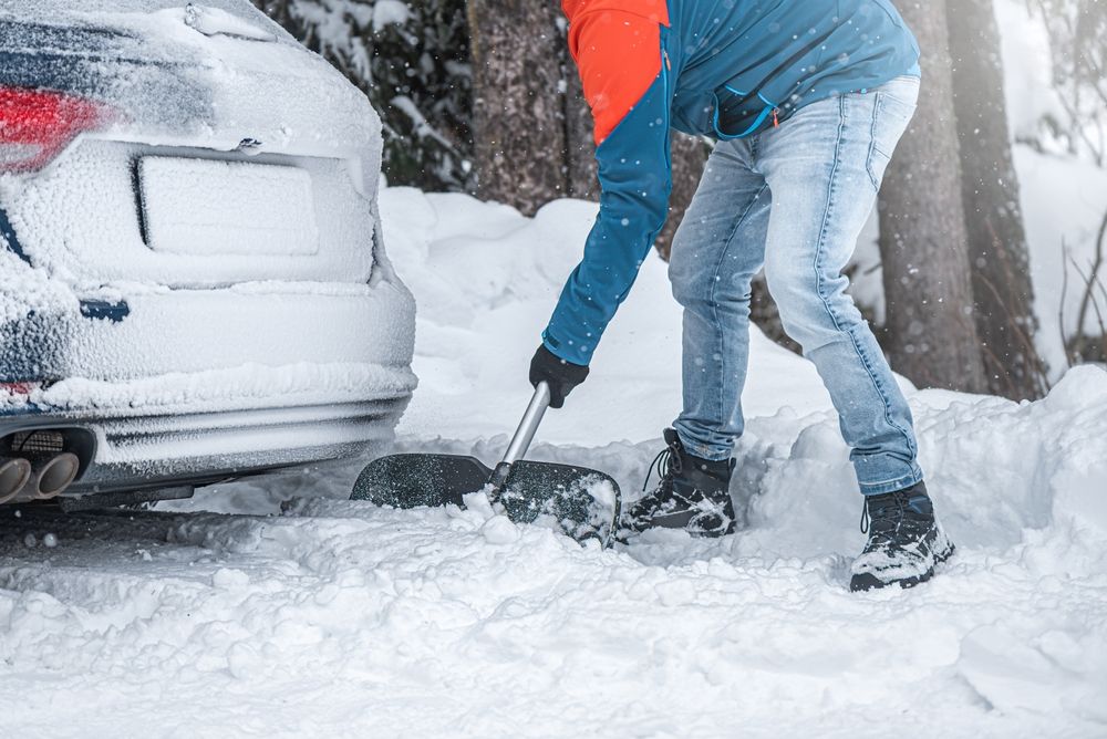 A remote worker shoveling heavy snow from a driveway next to a car in New Jersey, illustrating potential workers' compensation injury risks at home.
