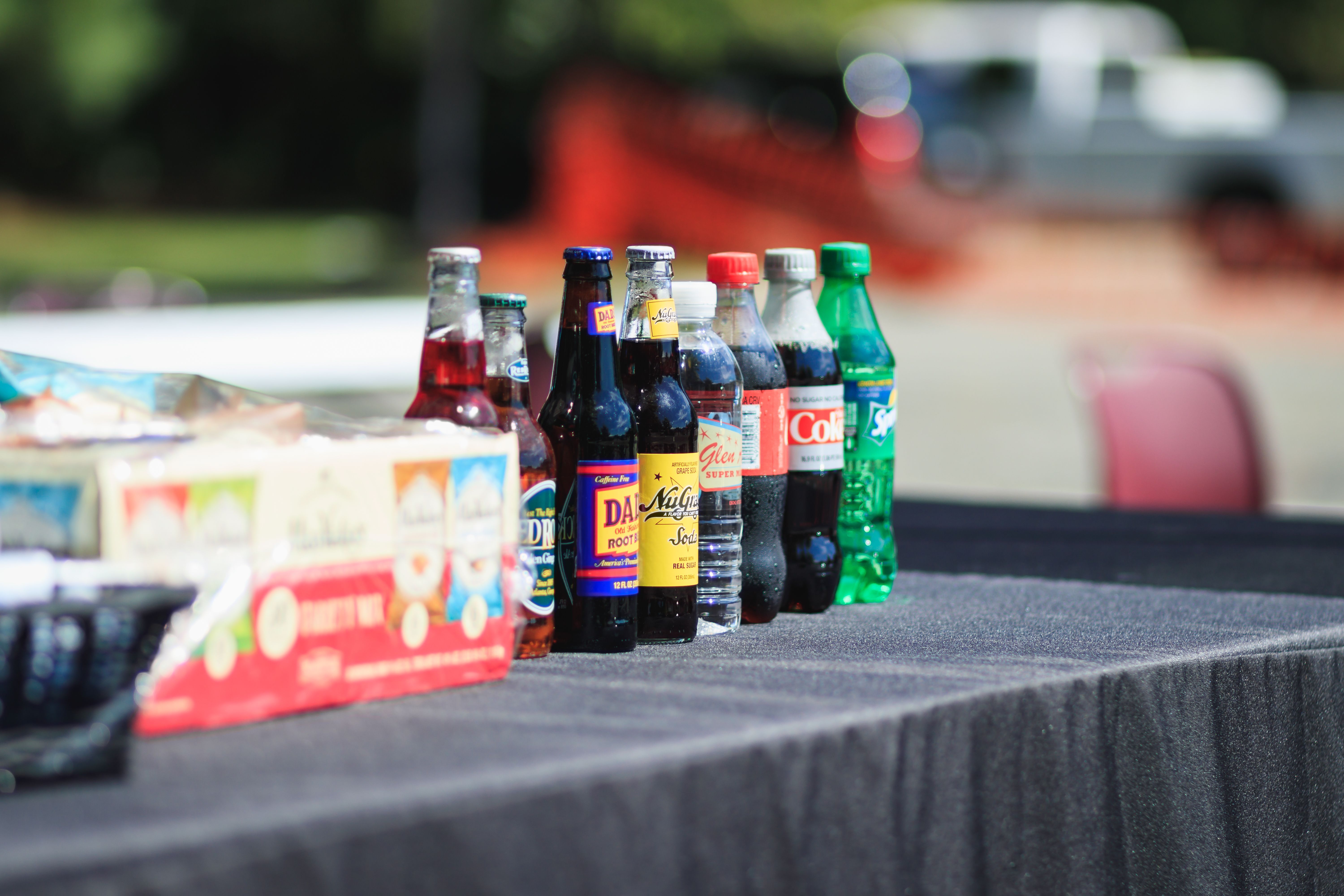 Assorted glass and plastic bottles of soda and beverages lined up on a table at an outdoor tailgate in New Jersey.