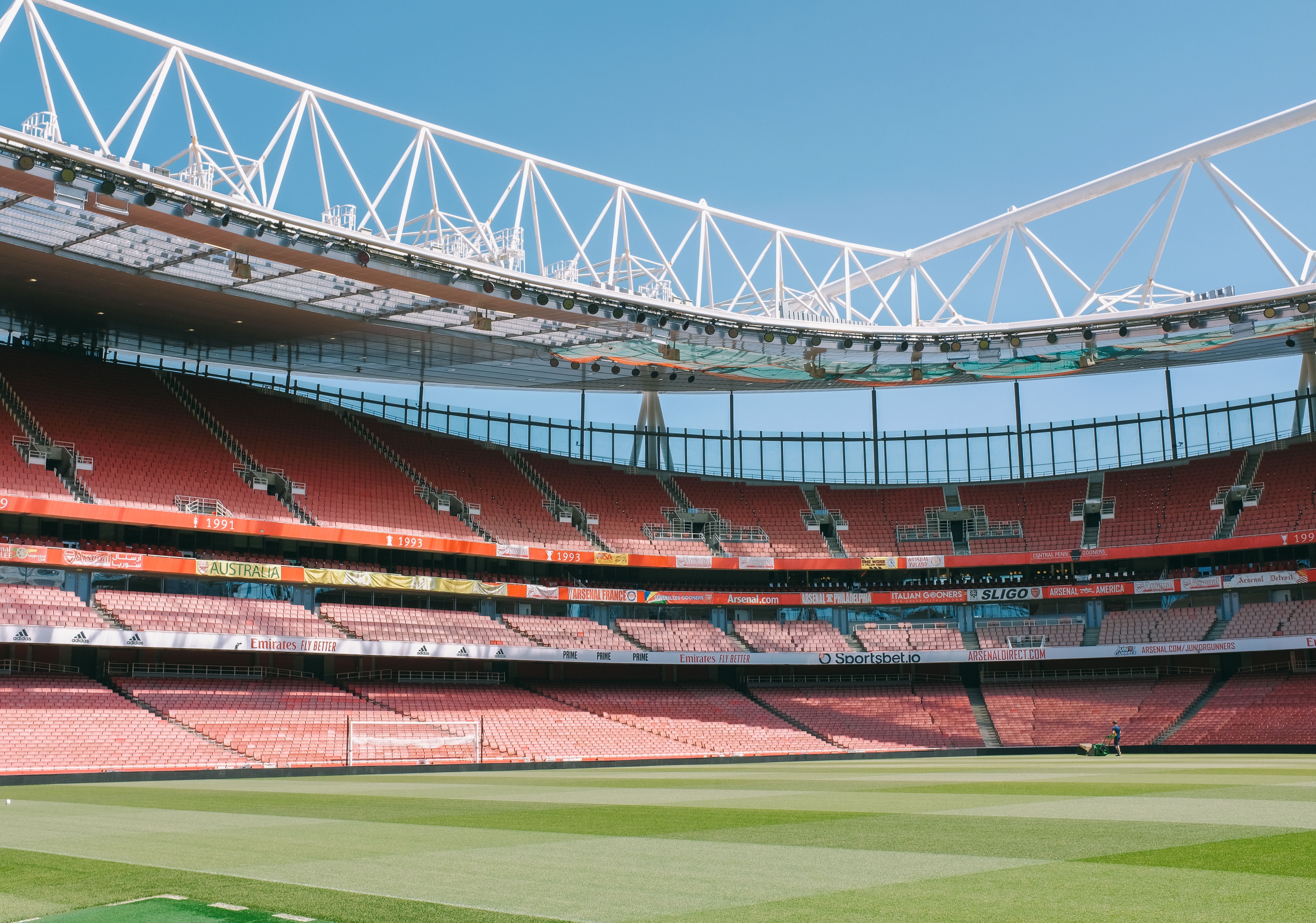 Image Rows of empty red seats surrounding the field inside a large sports stadium on a clear day.