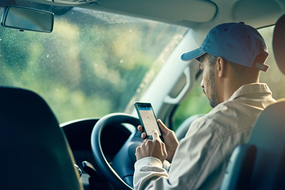 Delivery driver sitting behind the wheel and looking at a phone while parked, illustrating distracted driving risks during Thanksgiving weekend traffic in New Jersey.