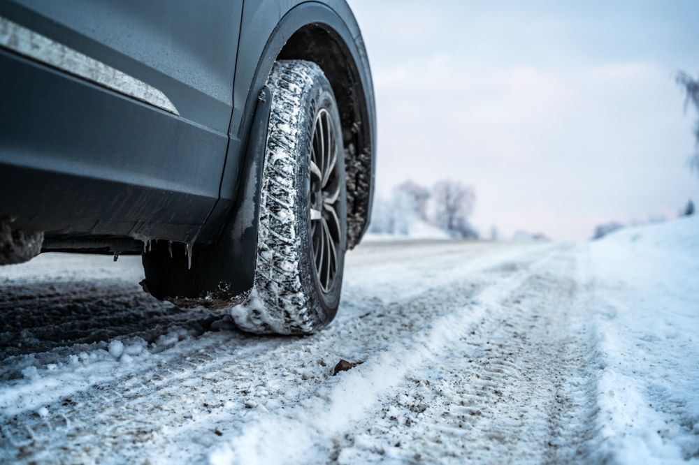 Close-up of a vehicle tire on a snow-covered road illustrating dangerous black ice conditions.