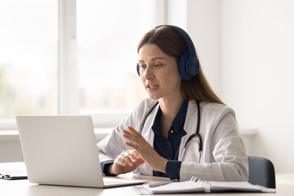 Professional female doctor wearing headphones and a white coat conducting a Zoom consultation to discuss medical diagnosis in New Jersey.