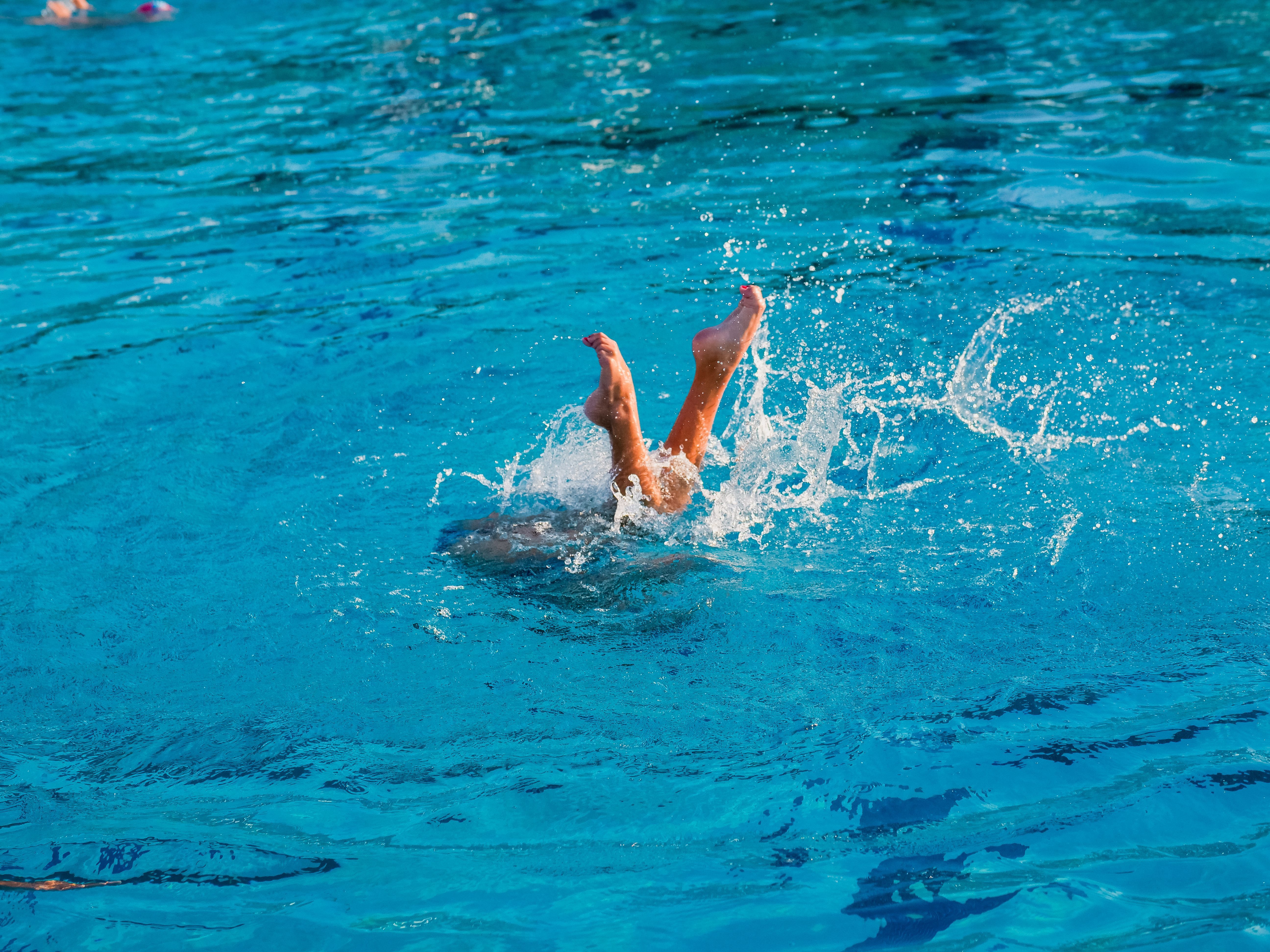 A swimmer's legs splashing above the surface of a bright blue outdoor swimming pool, illustrating pool accident and drowning risks in New Jersey.