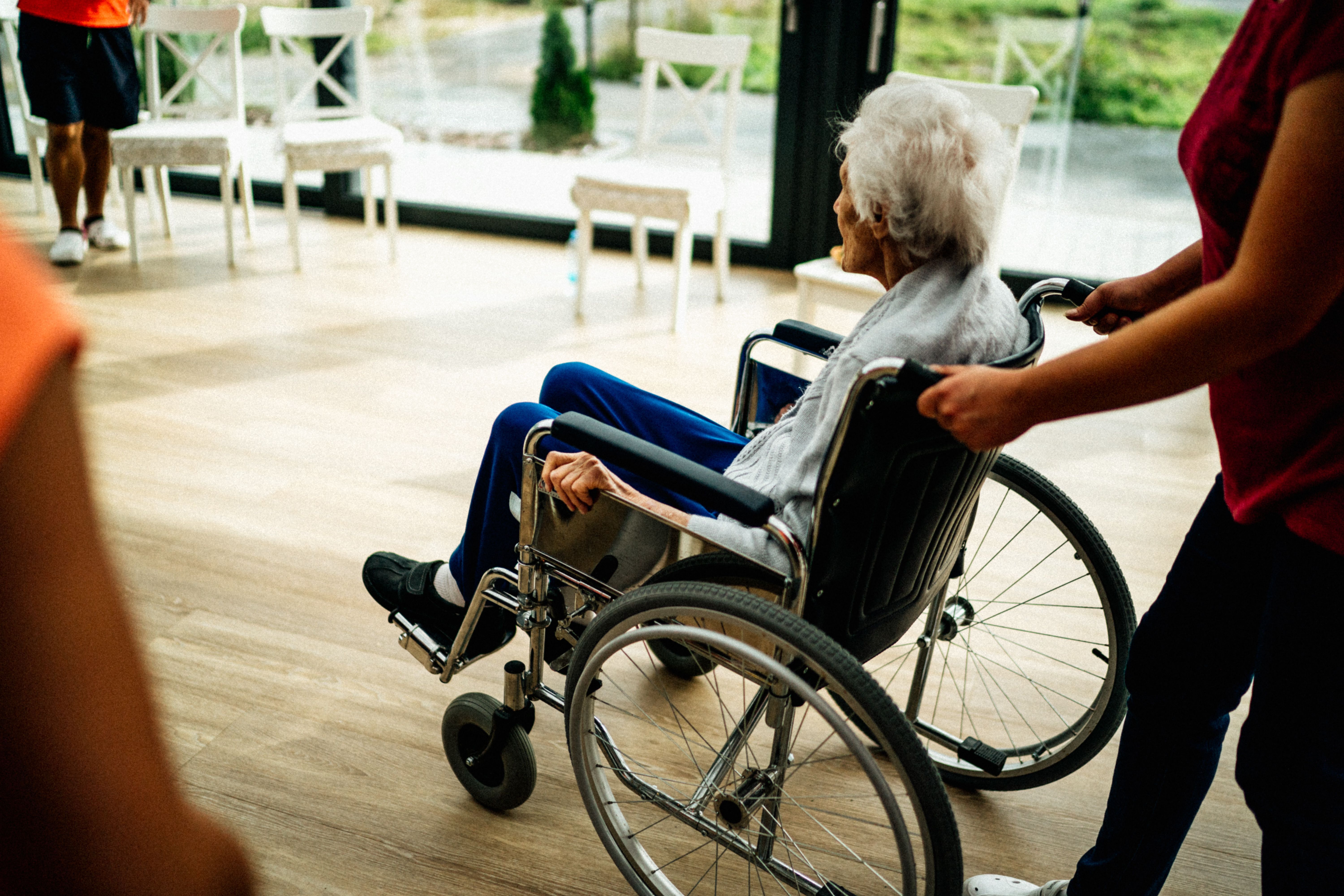 Caregiver pushing an elderly woman in a wheelchair inside a nursing home