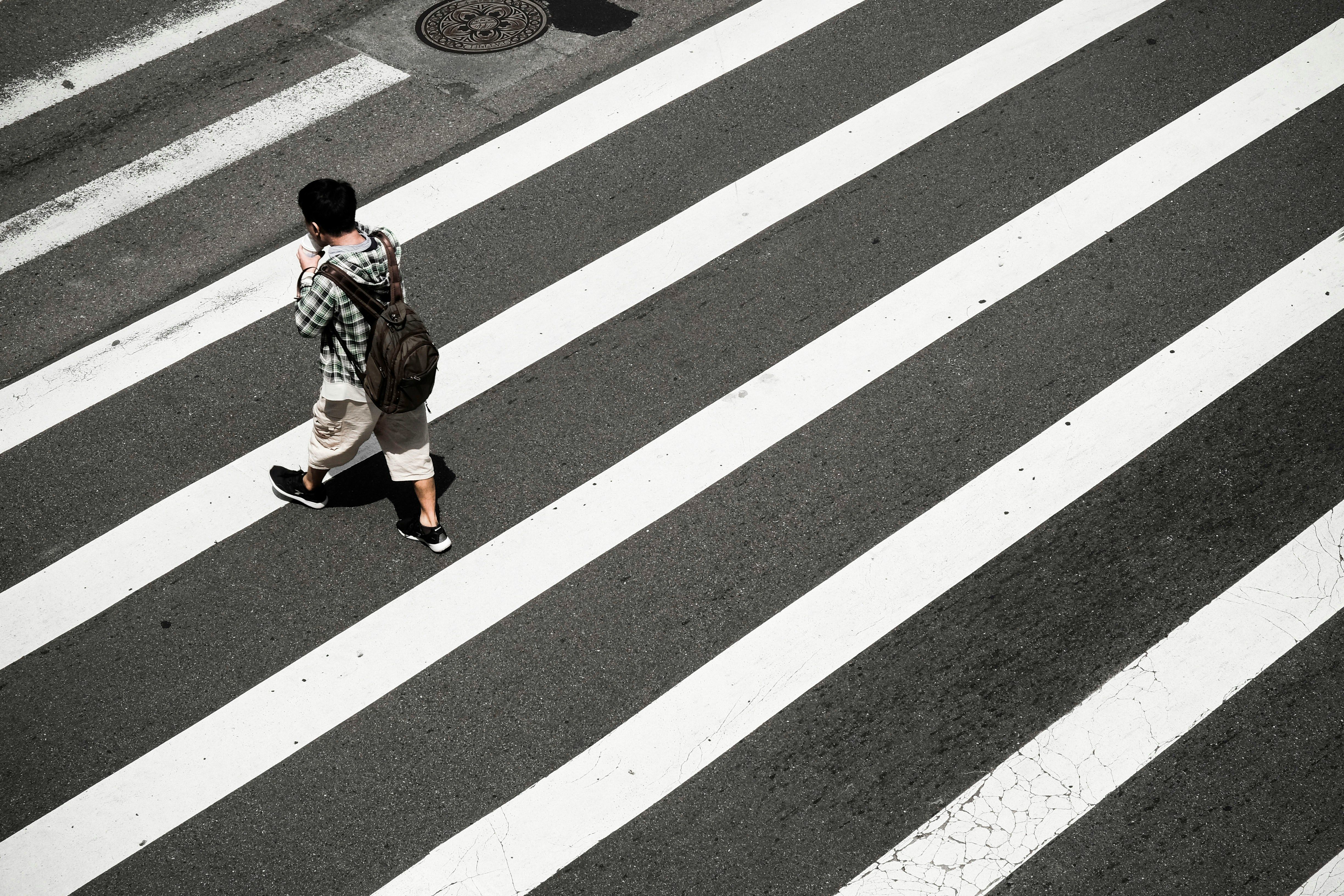 Pedestrian with a backpack walking across a city crosswalk, illustrating the risk of Newark pedestrian accidents.
