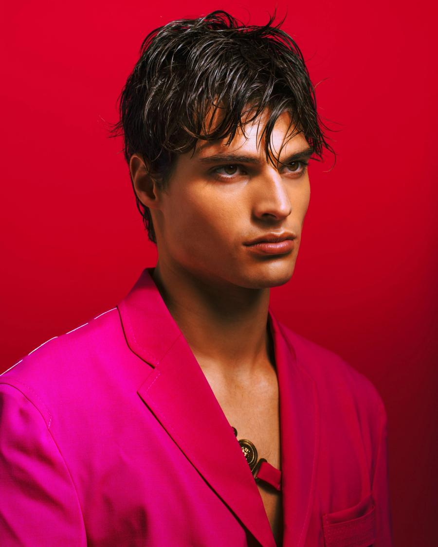 Cole Tallman with tousled wet hair in a hot pink blazer against a red backdrop, photographed by Taylor Miller.