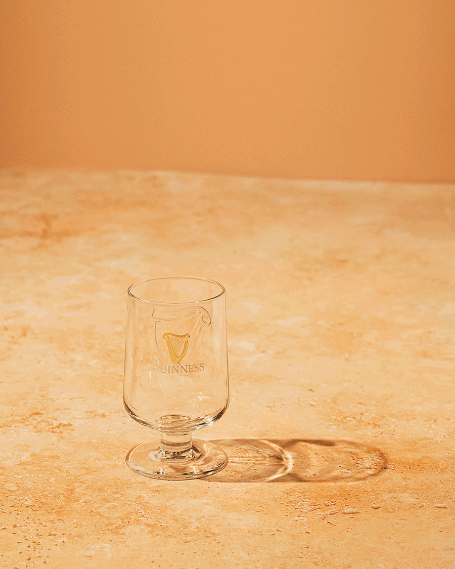 Warm toned stop motion of a Guinness Extra Stout bottle pouring into a glass held in hand, photographed by Taylor Miller.
