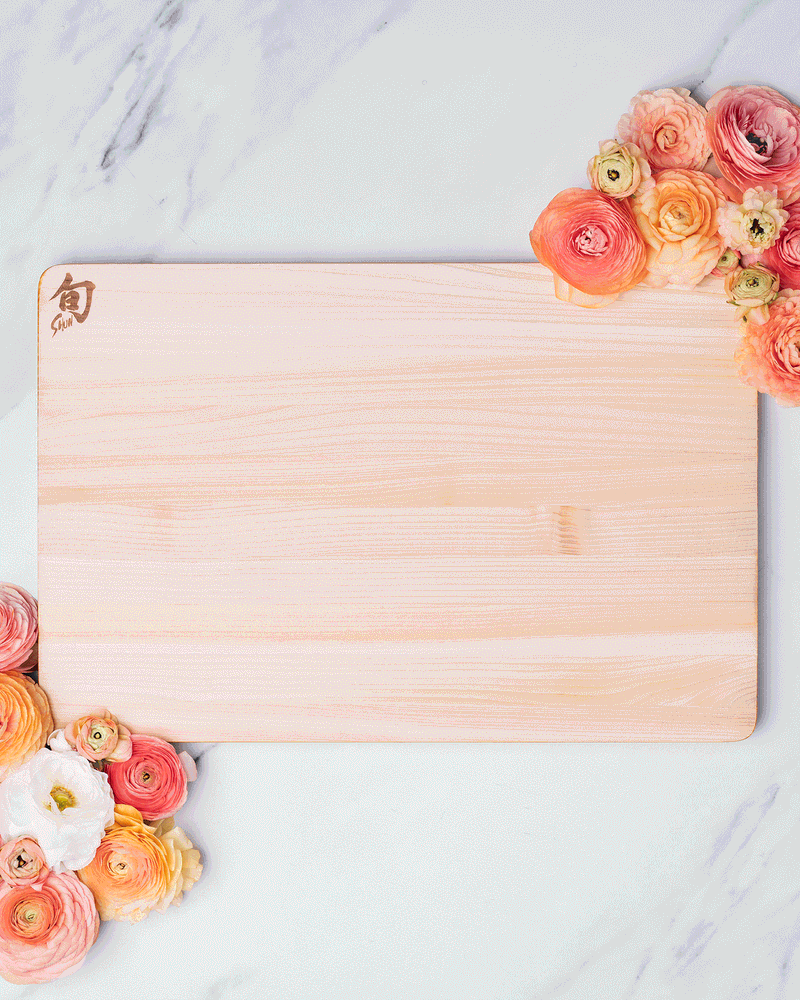 Overhead stop motion of a wooden cutting board and paring knife framed by peach roses on white marble, photographed by Taylor Miller.