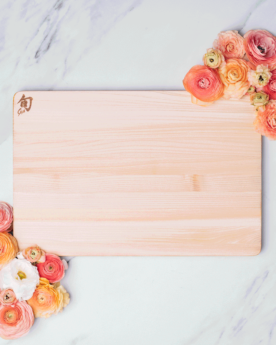 Overhead stop motion of a wooden cutting board and paring knife framed by peach roses on white marble, photographed by Taylor Miller.
