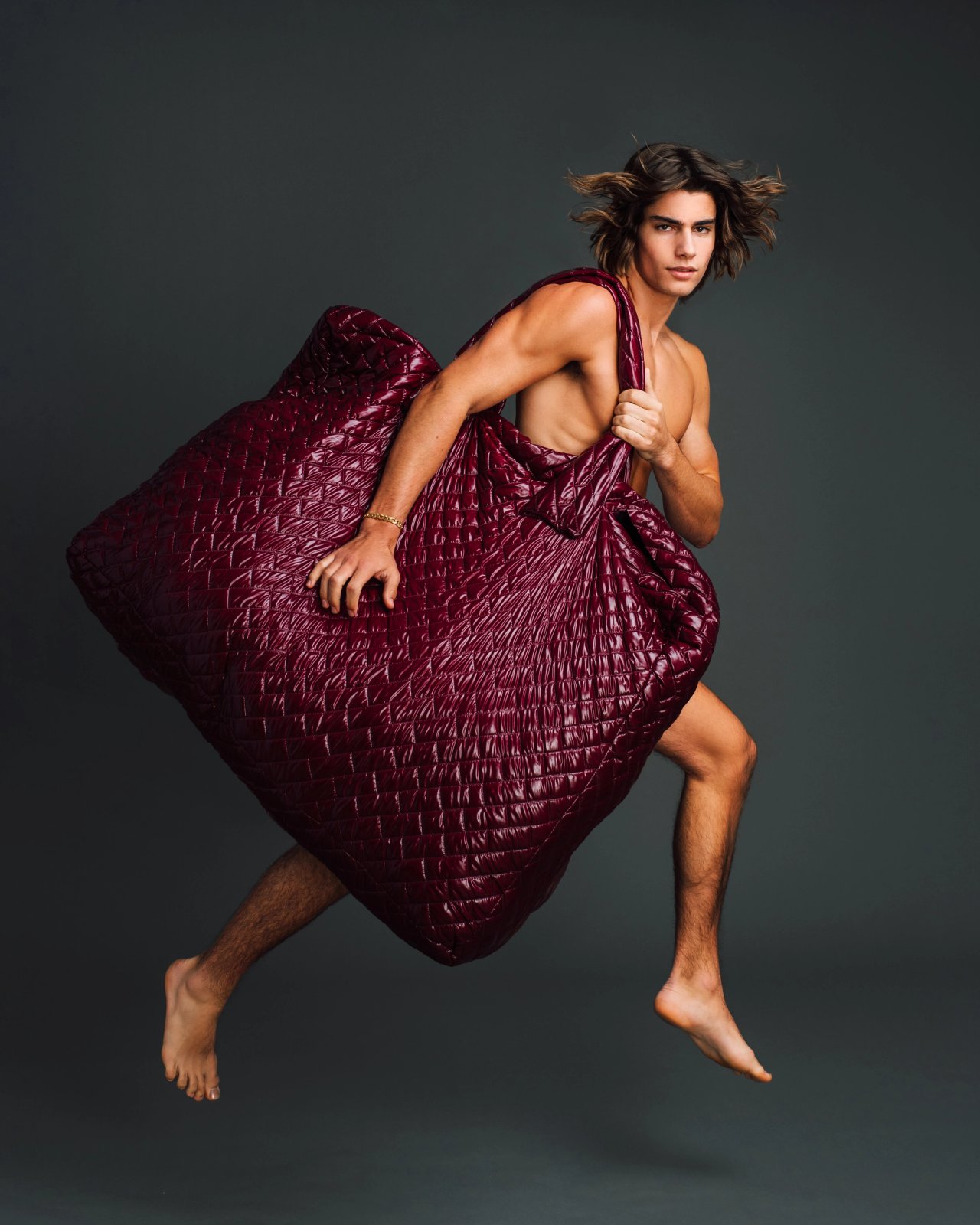 Model Corrado Martini, jumping with a large quilted bag, photographed for L'Officiel Hommes Poland shot by photographer Taylor Miller.