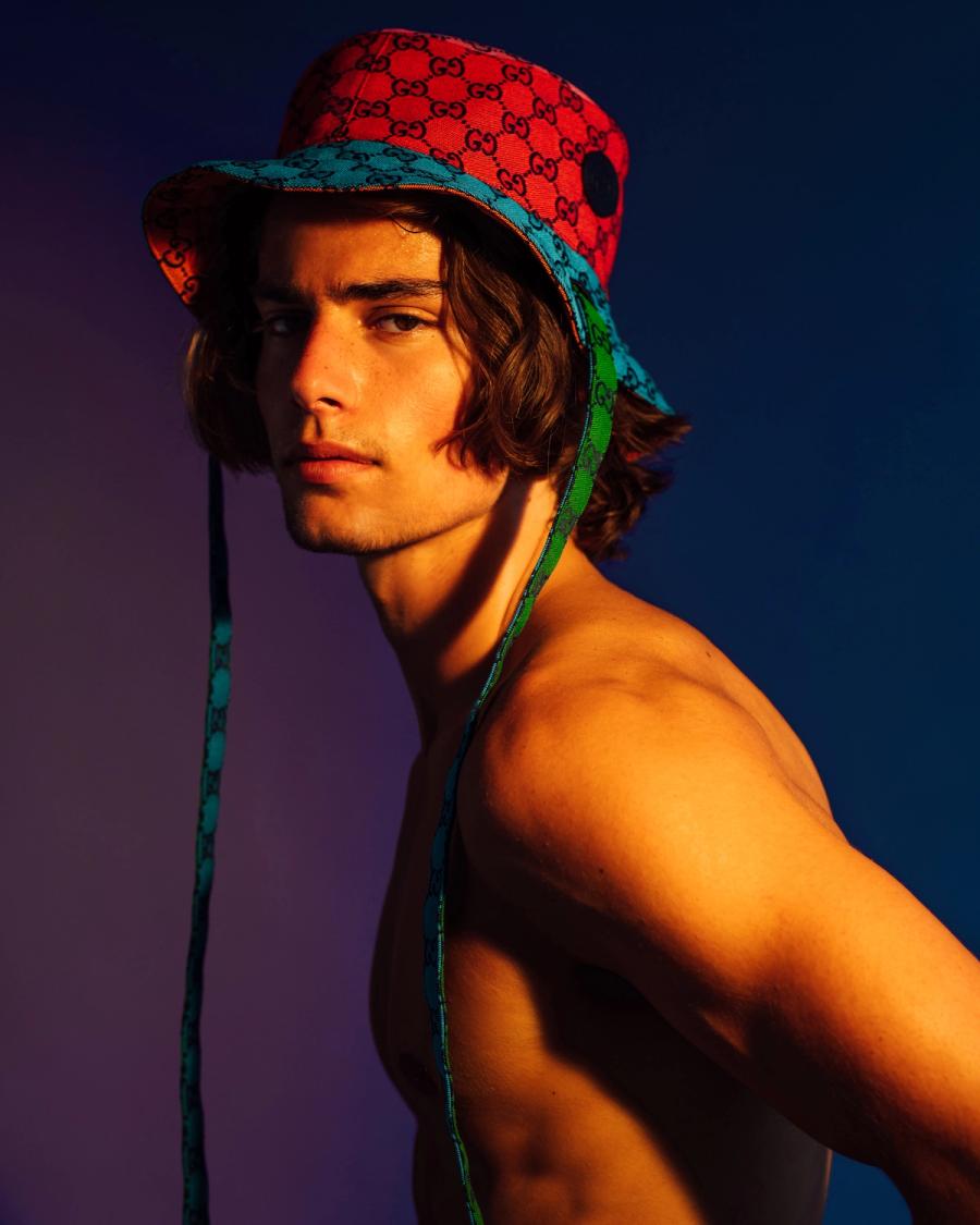 Corrado Martini wearing a red and blue Gucci monogram bucket hat under moody lighting, photographed by Taylor Miller.