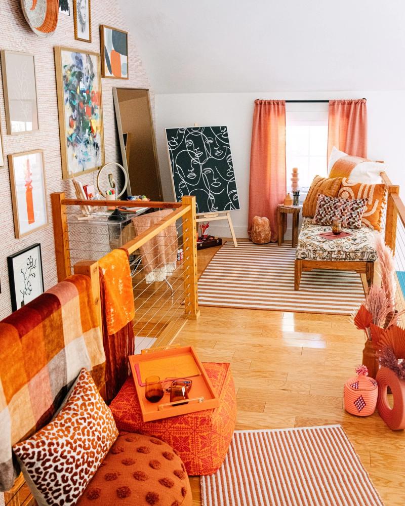 Sunlit loft in warm orange HomeGoods decor with framed art, a line-drawing canvas and striped rugs, styled for BuzzFeed by photographer Taylor Miller.