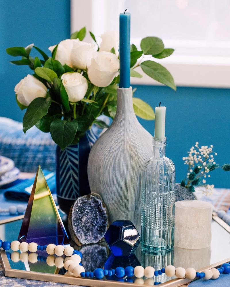 Mirrored-tray vignette of HomeGoods vases, taper candles and white roses in blue tones, styled for BuzzFeed by photographer Taylor Miller.