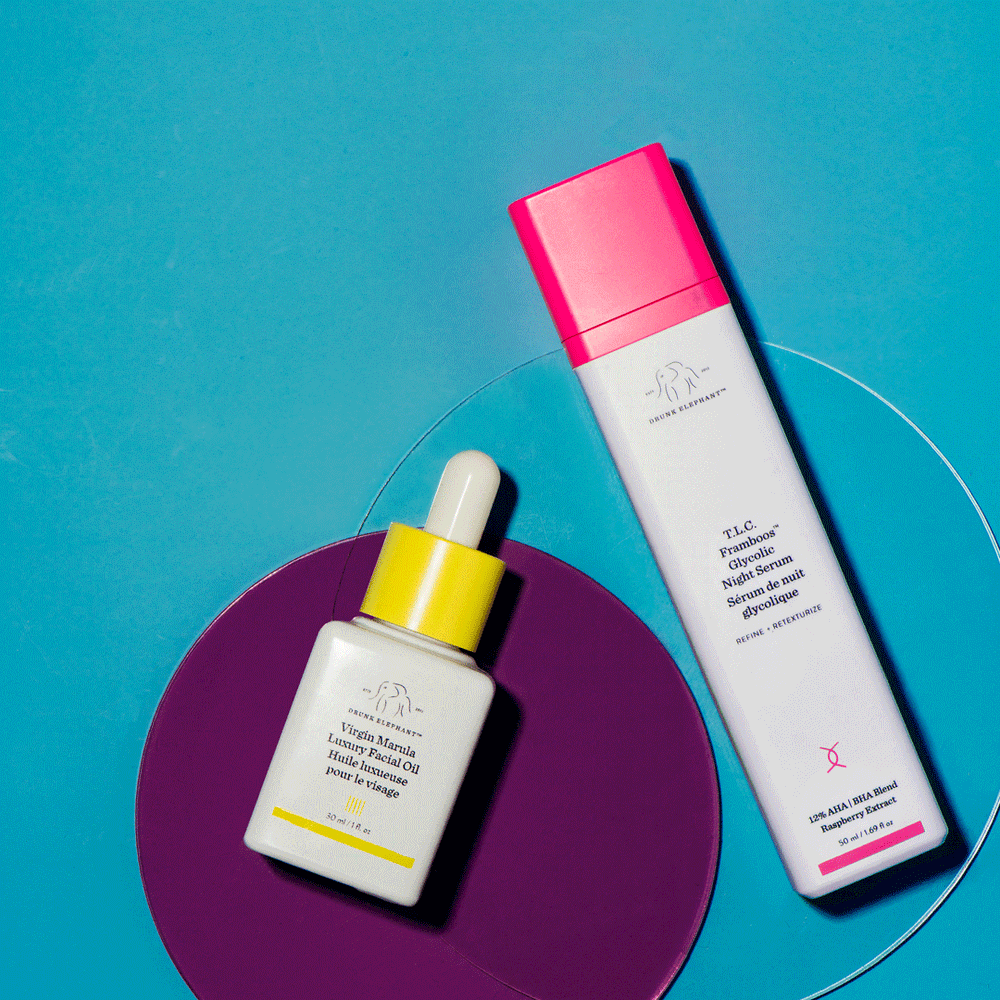Colorful Drunk Elephant skincare flat lay with a Virgin Marula oil dropper and a tube on a teal and purple set, photographed by Taylor Miller.