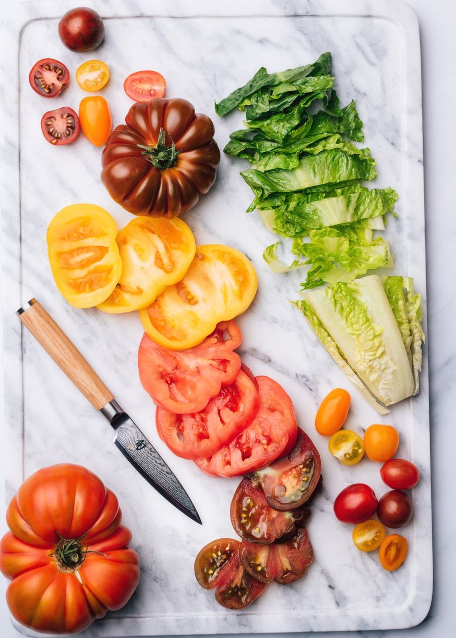 Kai damascus knife on a marble board with sliced red and yellow heirloom tomatoes and chopped romaine lettuce, photographed for BuzzFeed by Taylor Miller.