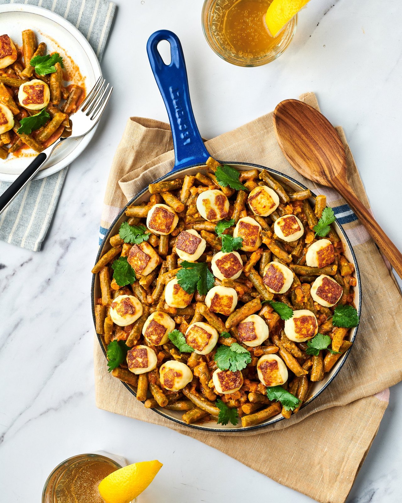 Blue skillet of green beans with seared halloumi and cilantro, plated portion and lemon nearby, for Libby's and BuzzFeed by Taylor Miller.