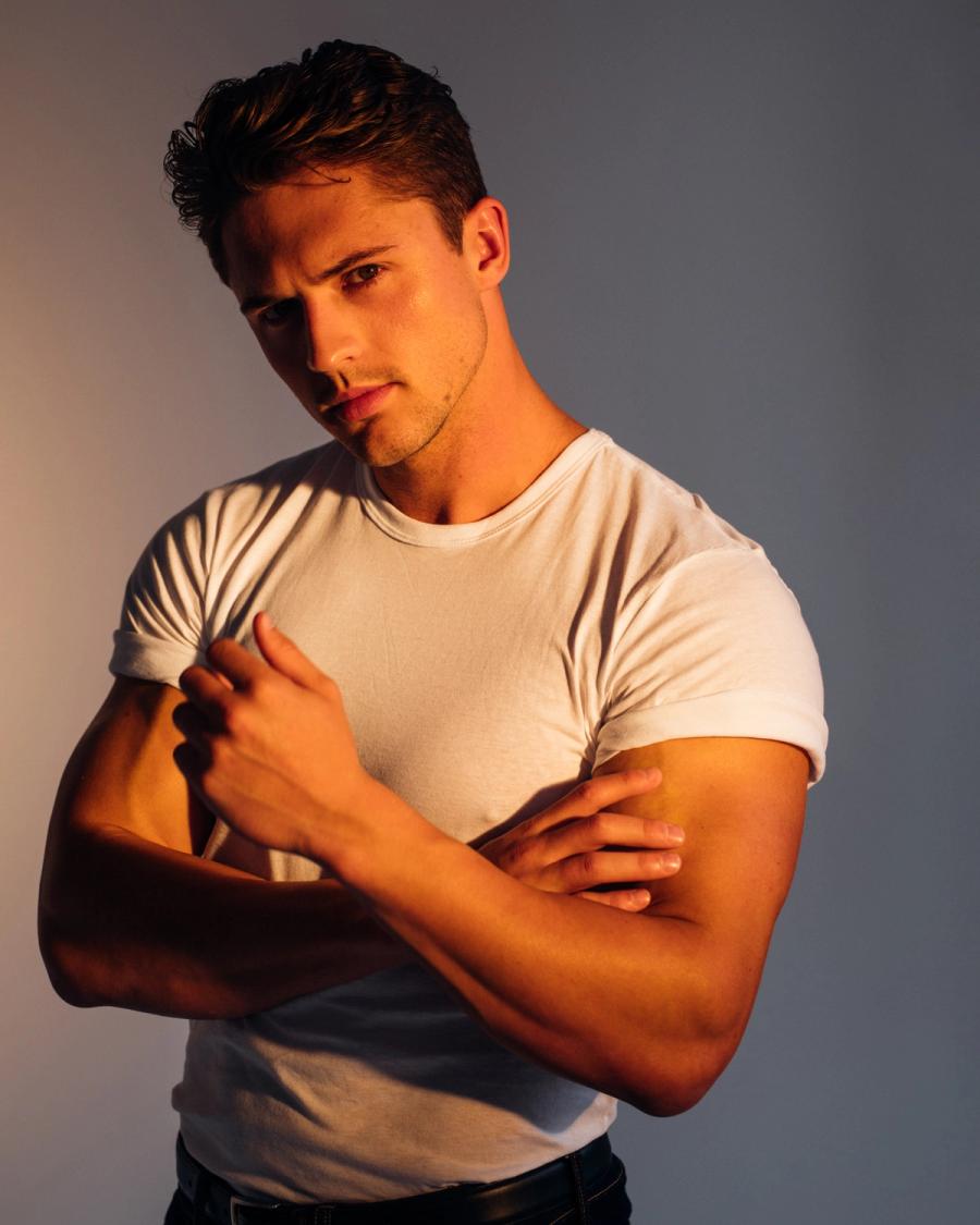 Nick Topel in a fitted white t-shirt with rolled sleeves posing in warm studio light, photographed by Taylor Miller.