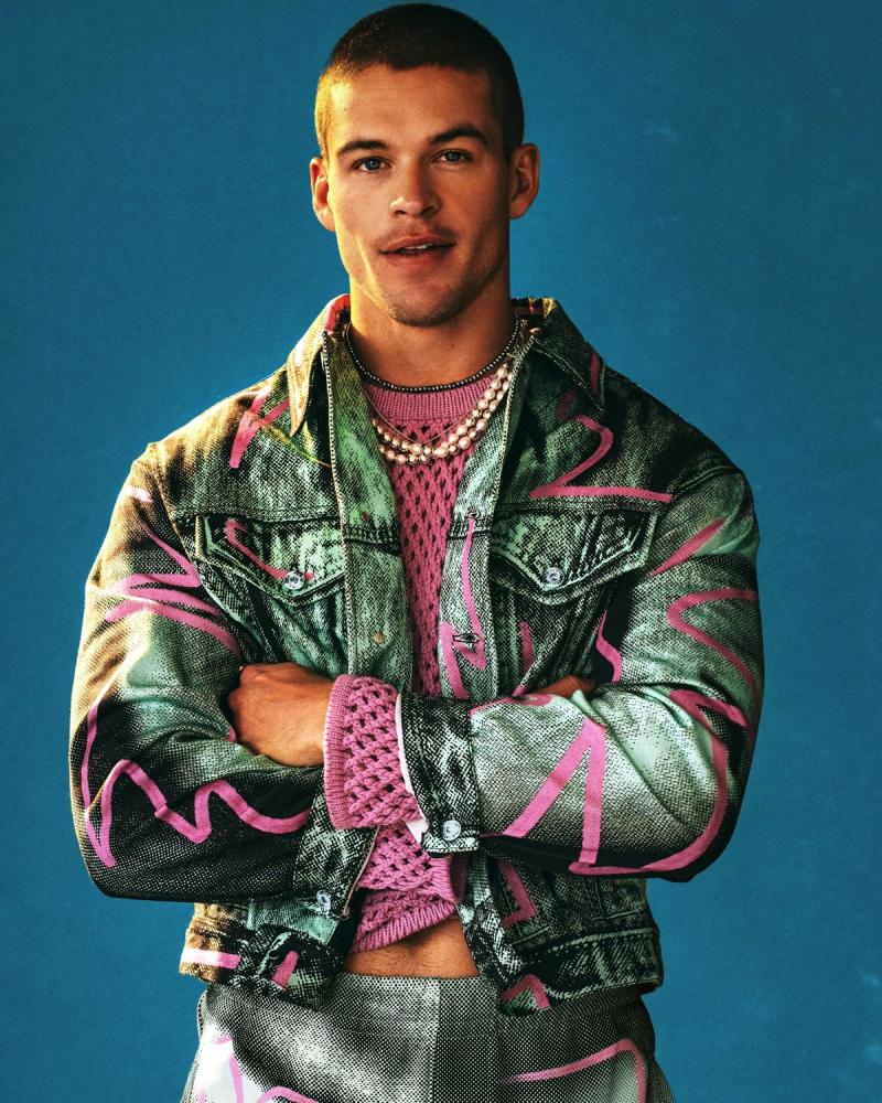 Model Mitchell Slaggert in a graffiti-printed denim jacket over a pink crochet top, arms crossed against a teal backdrop for Numéro Netherlands, photographed by Taylor Miller.