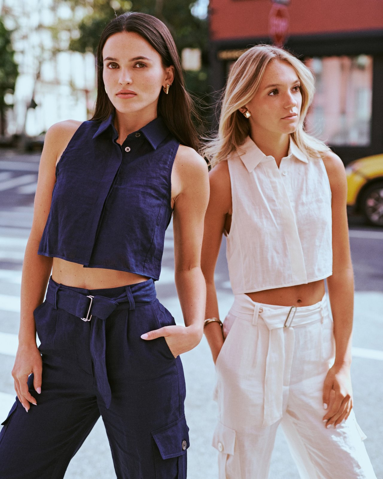 Mary Holland Nader and Julia Lisboa in navy and cream linen crop-top and trouser sets crossing a city street for the ESYA editorial campaign, photographed by Taylor Miller.