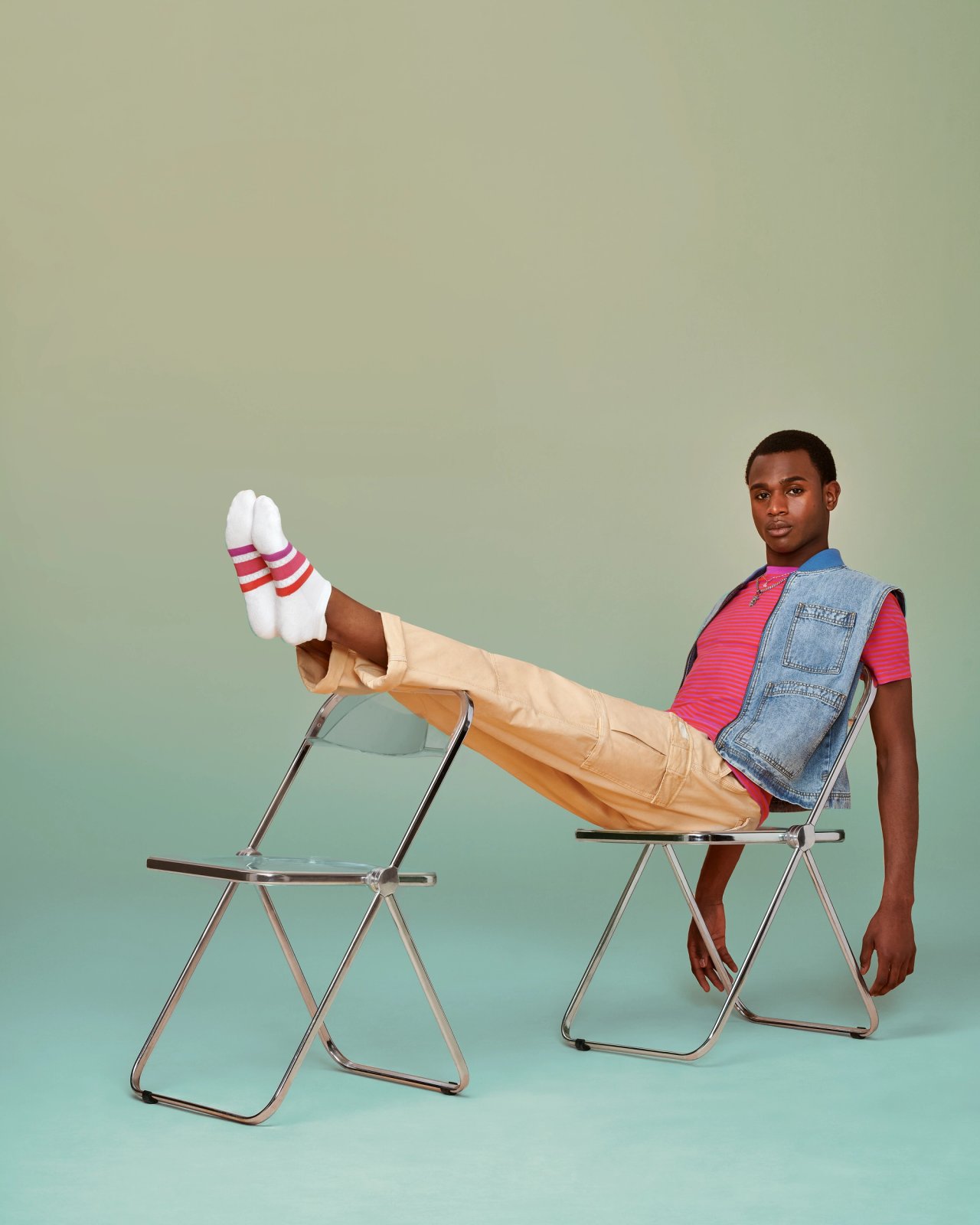 Four Dorzelma reclines across two folding chairs, feet up in white Bombas socks with pink and red stripes, photographed for Bombas Pride 2024 by Taylor Miller.