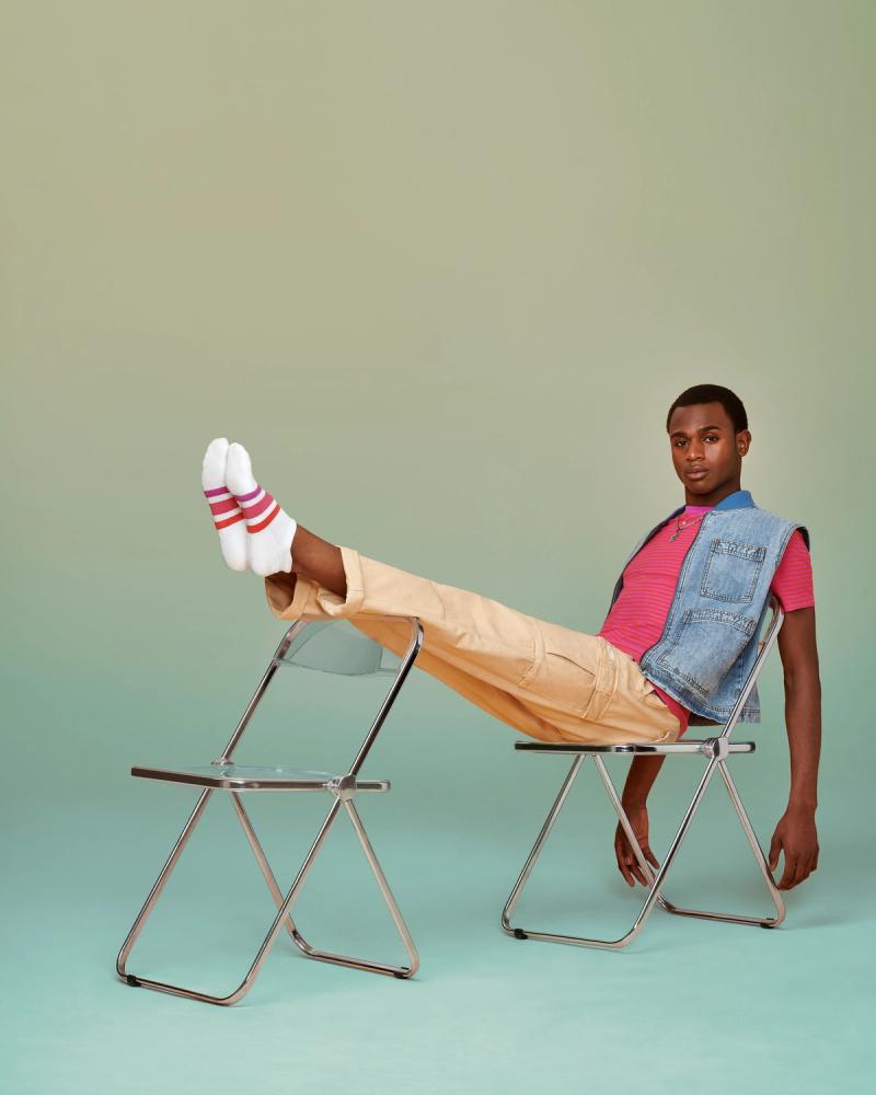 Four Dorzelma reclines across two folding chairs, feet up in white Bombas socks with pink and red stripes, photographed for Bombas Pride 2024 by Taylor Miller.