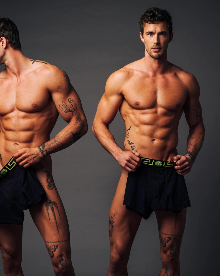 Christian Hogue, shirtless and tattooed in navy Versace boxer shorts, in a side-by-side studio portrait, photographed by Taylor Miller.