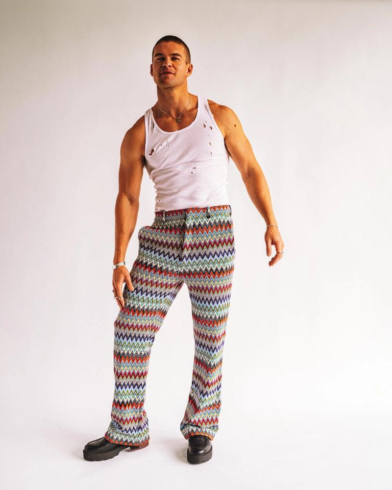 Mitchell Slaggert in a distressed white tank top and colorful zigzag knit trousers with chunky black boots, photographed for Numéro Netherlands by Taylor Miller.