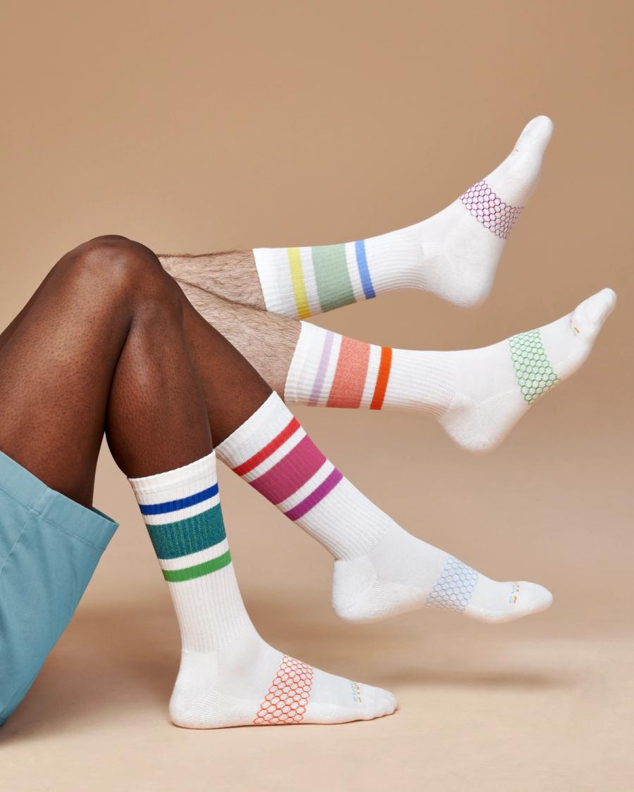 White Bombas crew socks with multicolored Pride stripes worn on several legs, photographed for the Bombas Pride 2024 campaign by Taylor Miller.