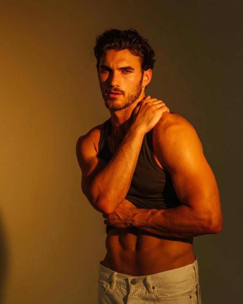 Warmly lit portrait of Michael Yerger in a dark tank top and white jeans for L'Officiel Hommes, photographed by Taylor Miller.