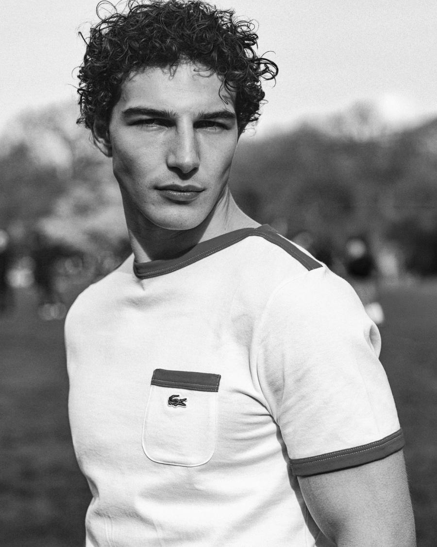 Black and white park portrait of Sacha Bilal in a white Lacoste pocket tee, for the Lacoste NYC 2026 campaign by Taylor Miller.
